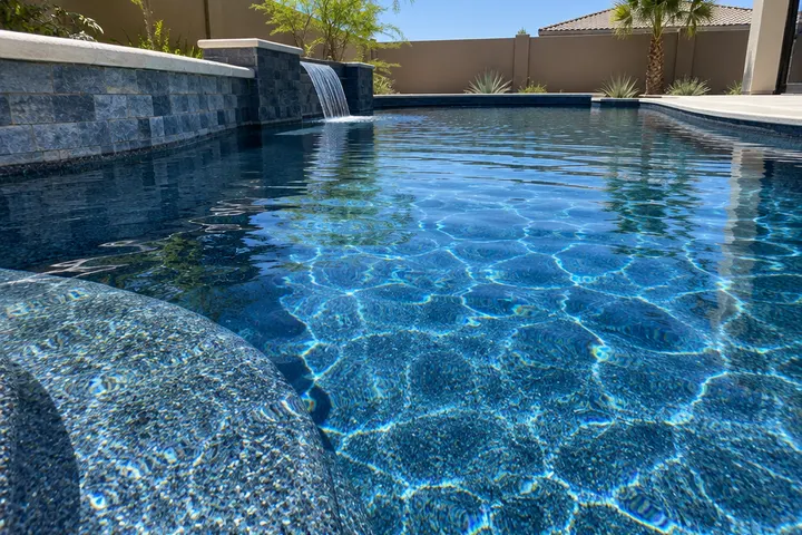 Close-up of a new midnight-blue pebble pool finish under clear sparkling water with sunlight ripples